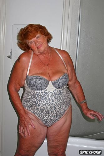 self assured elderly ssbbw super sized big beautiful woman granny senior ninety of age stands in bathroom in one piece swimsuit permed ginger hair her full